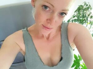 Frau mit hellem Teint und zurückgebundenen Haaren macht ein Selfie und blickt direkt in die Kamera.